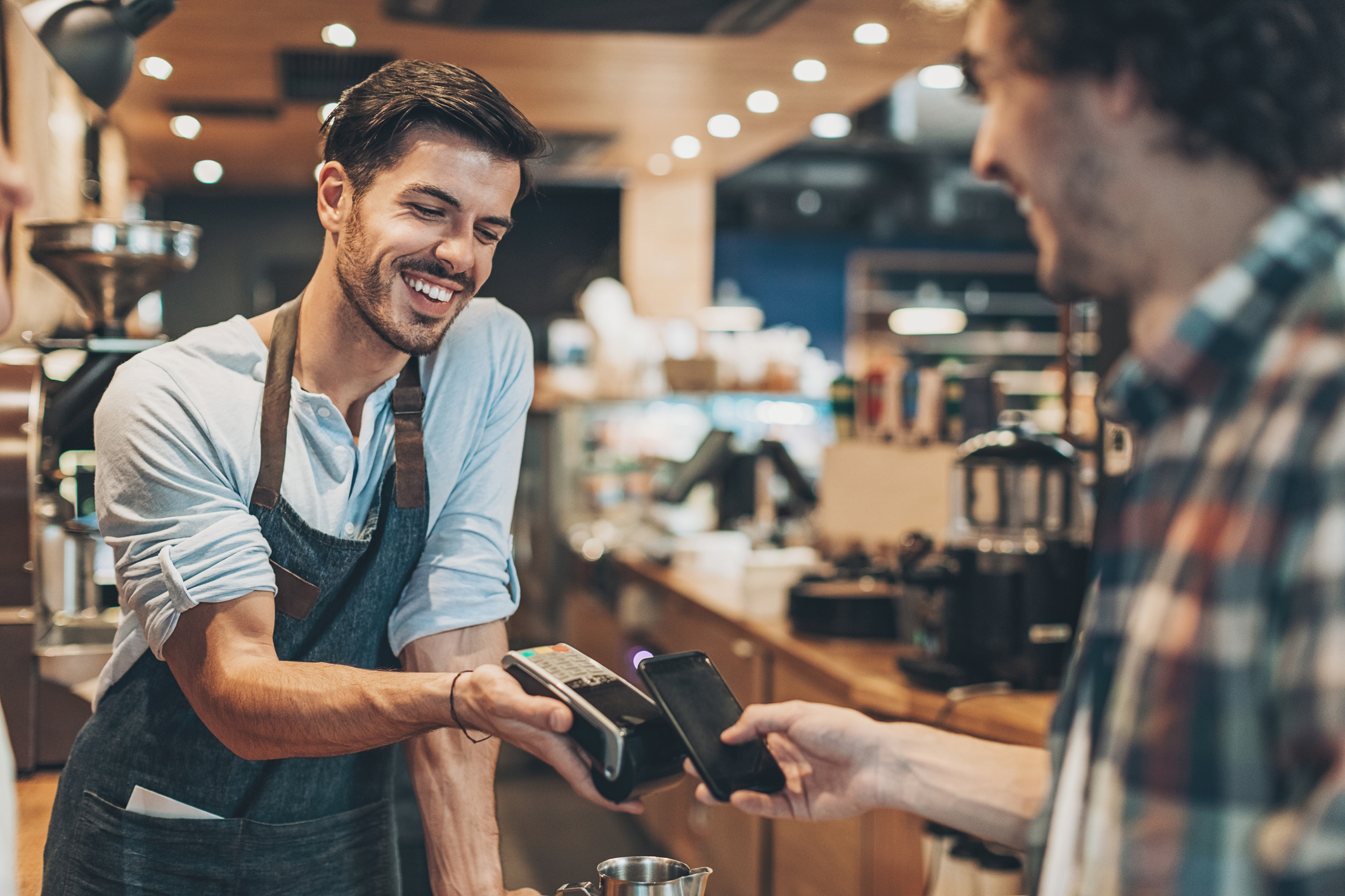 Smiling barista with barcore reader accepting smart phone payment